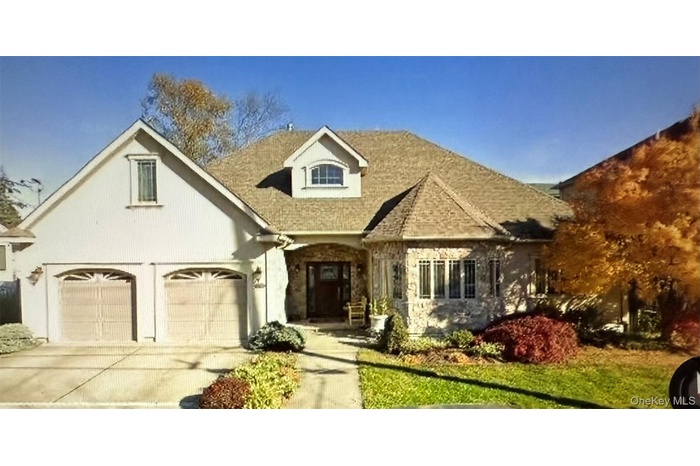 View of front facade featuring driveway, stone siding, a front lawn, and stucco siding