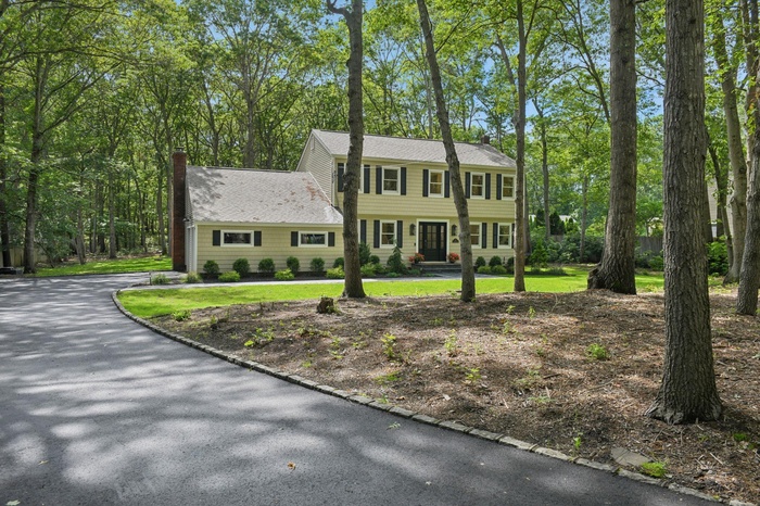 Colonial home featuring a chimney, a shingled roof, and a front yard