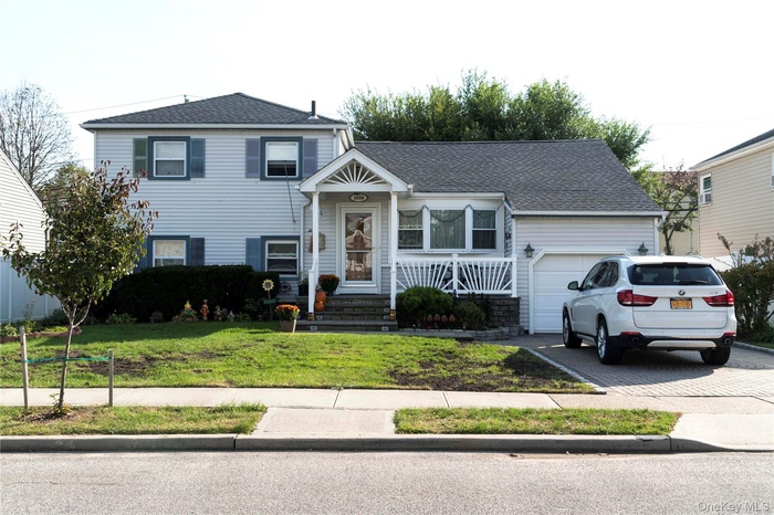 Split level home with roof with shingles, a front lawn, a garage, and driveway