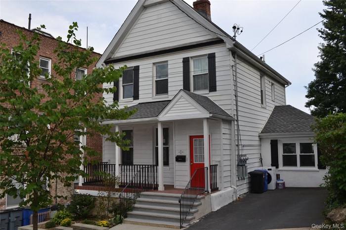 View of front facade with roof shingles, covered porch, and a chimney