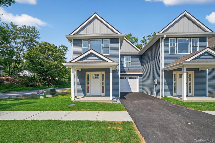 View of front of property with board and batten siding, a porch, asphalt driveway, a front lawn, and an attached garage