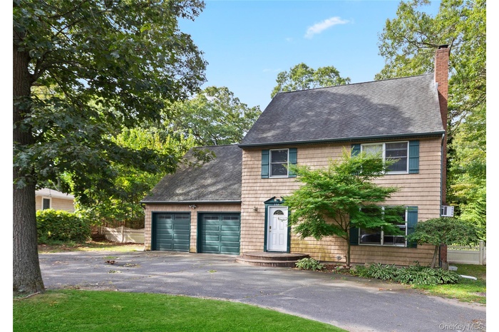 Colonial home with a shingled roof, a chimney, driveway, and a garage
