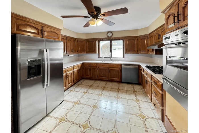 Kitchen featuring stainless steel appliances, light countertops, a ceiling fan, and brown cabinetry