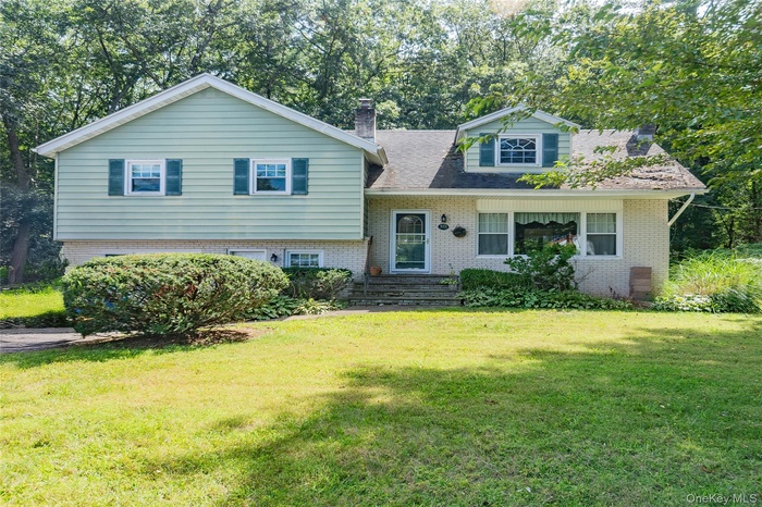 Split level home featuring brick siding, a chimney, and a front lawn
