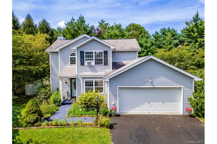 Traditional home with driveway, roof with shingles, a chimney, and an attached garage