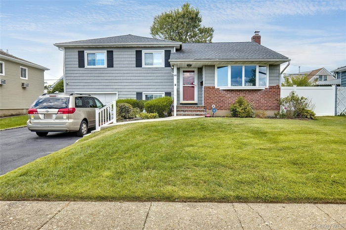 Tri-level home featuring driveway, a chimney, a shingled roof, brick siding, and an attached garage