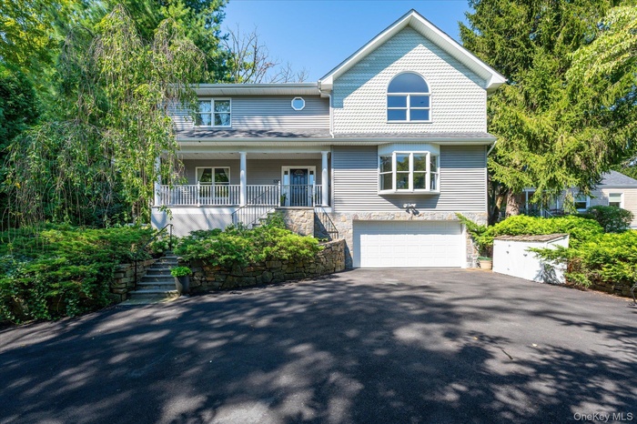 View of front of home with driveway, a porch, stone siding, and an attached garage.