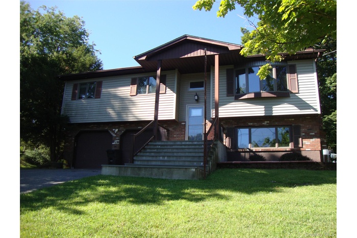 Raised ranch with a front lawn, driveway, stairs, and an attached garage