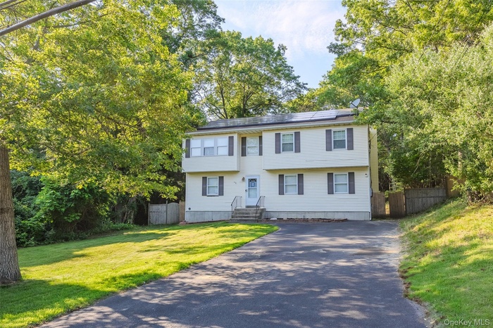 Colonial inspired home with driveway, solar panels, and view of scattered trees