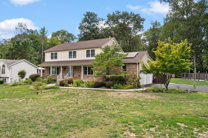 Traditional-style home featuring covered porch, a front yard, solar panels, brick siding, and roof with shingles