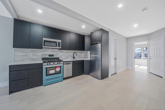 Kitchen with tasteful backsplash, appliances with stainless steel finishes, light wood-type flooring, modern cabinets, and dark cabinets