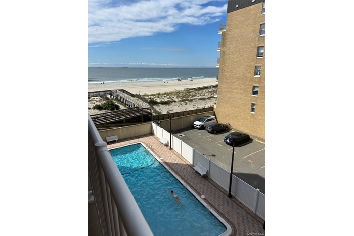 Community pool featuring a fenced backyard, view of water and beach, and a balcony