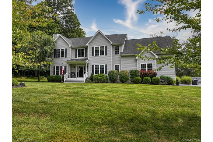 View of front facade featuring a shingled roof, a front lawn, covered porch, and a chimney