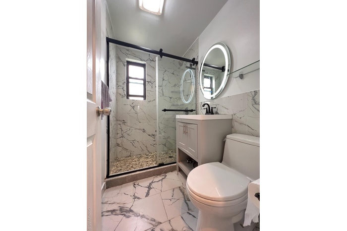 Bathroom featuring light marble finish flooring, a marble finish shower, vanity, and tile walls