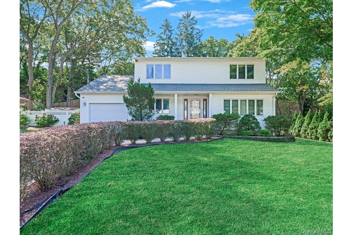 Traditional-style home featuring a front yard, an attached garage, and covered porch
