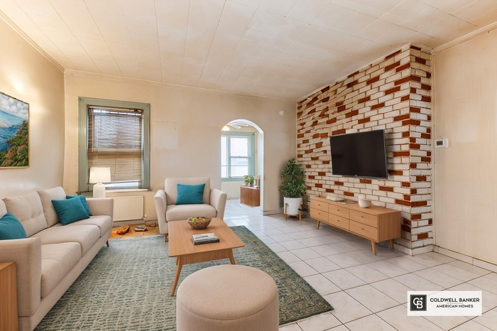 Living area with radiator, light tile patterned floors, arched walkways, and crown molding