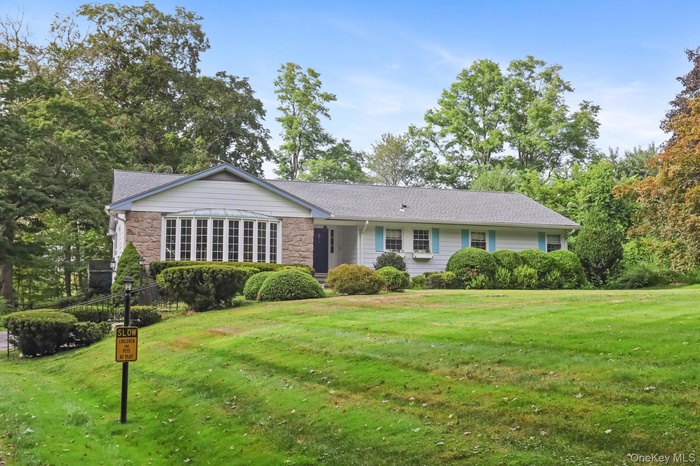 Ranch-style home with stone siding, a front yard, roof with shingles, and view of wooded area