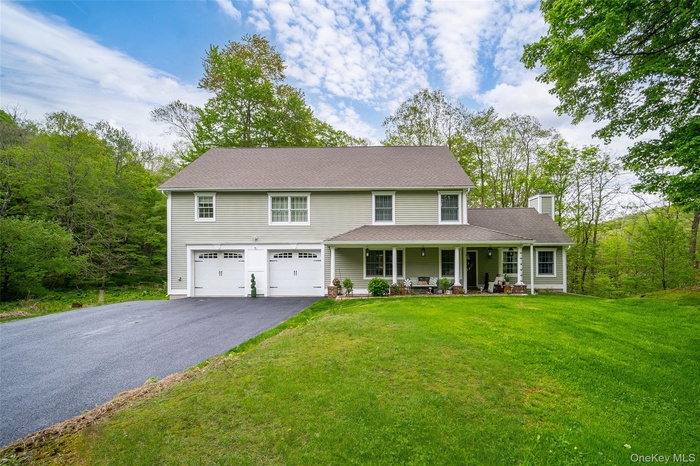 View of front of property with asphalt driveway, a porch, a chimney, an attached garage, and a front yard