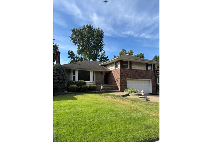 Tri-level home with brick siding, concrete driveway, a front yard, and an attached garage