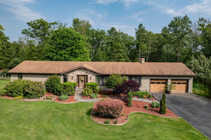 Ranch-style house with an attached garage, driveway, a front yard, a chimney, and stone siding
