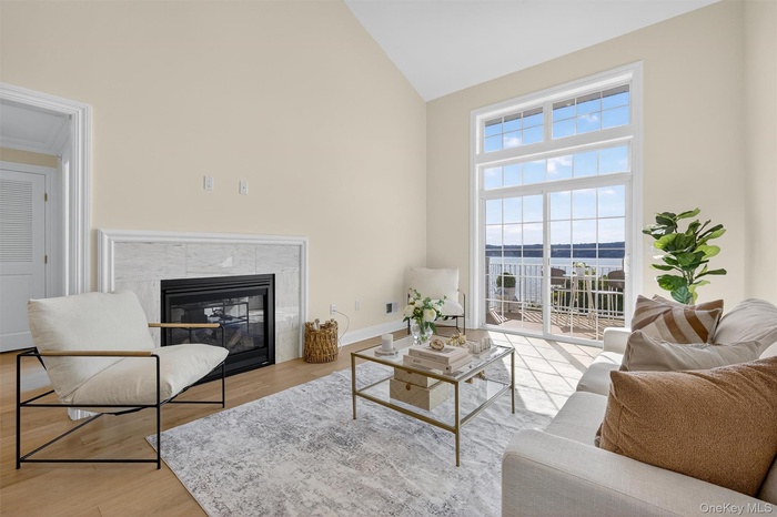 Living room with vaulted ceiling, marble gas fireplace, light hardwood floors, and floor-to-ceiling sliding doors showcasing Hudson River views.