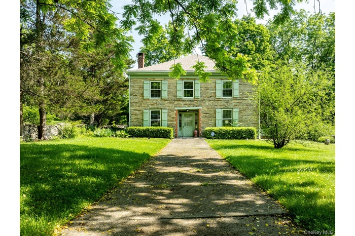 Colonial-style house with driveway, a chimney, stone siding, and a front yard