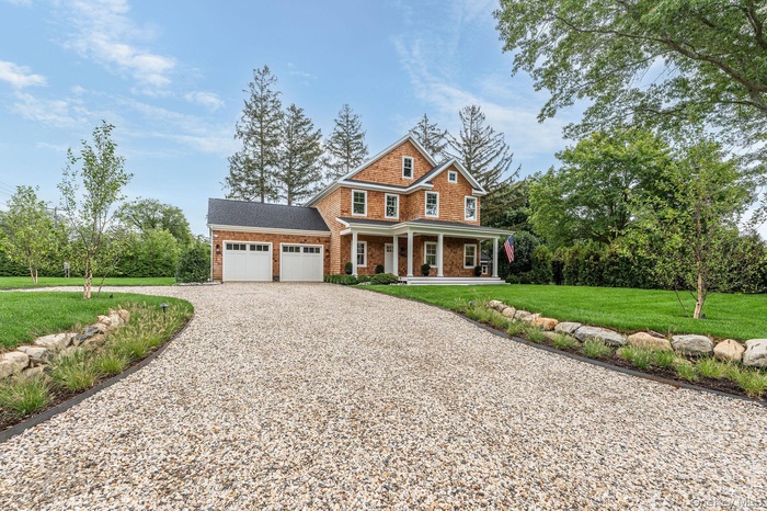View of front of home featuring driveway, covered porch, a front lawn, roof with shingles, and an attached garage