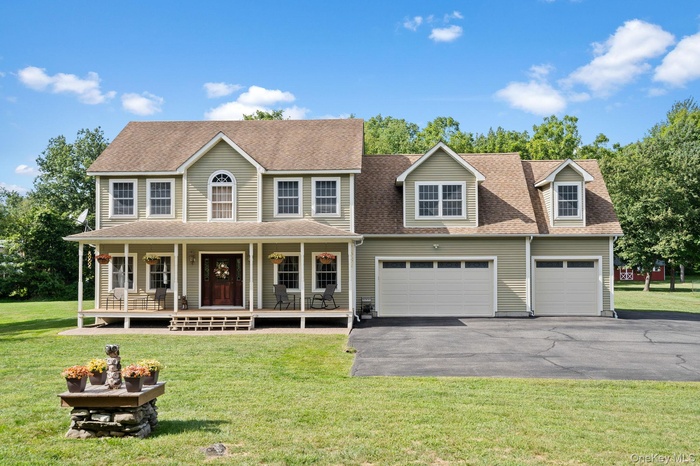 Colonial-style house featuring driveway, covered porch, a shingled roof, and a front lawn