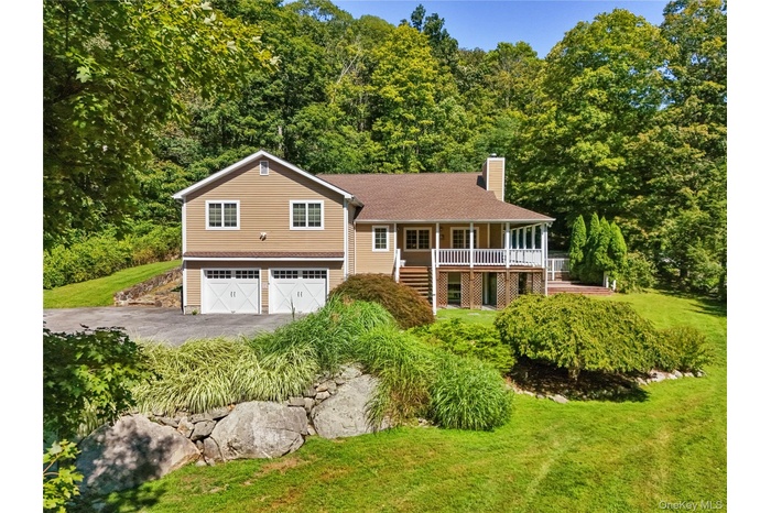 Split level home featuring asphalt driveway, a chimney, a porch, and a front lawn