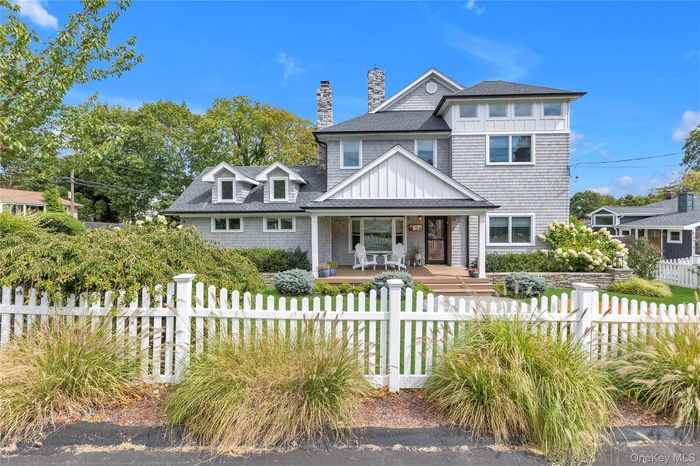 View of front of house with covered porch, a shingled roof, a fenced front yard, a chimney, and board and batten siding