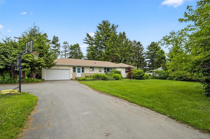 Ranch-style house featuring asphalt driveway, an attached garage, and a front lawn