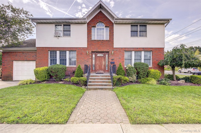 Traditional-style home featuring a front yard, brick siding, and an attached garage