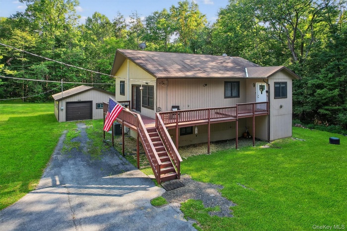 View of front of house with an outdoor structure, asphalt driveway, a detached garage, a shingled roof, and a wooden deck