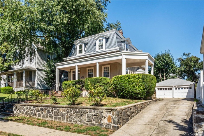 View of front of property featuring an outbuilding, a detached garage, a large porch, mansard roof, and a chimney