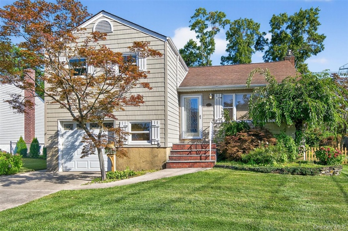 Split level home with a front yard, a chimney, concrete driveway, a garage, and a shingled roof