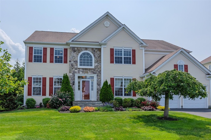 Colonial inspired home with a front yard, asphalt driveway, and stone siding