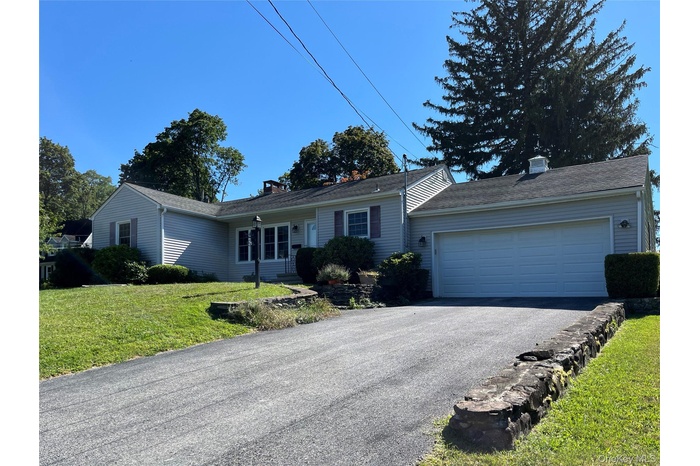 Single story home with a front yard, a chimney, driveway, and an attached garage