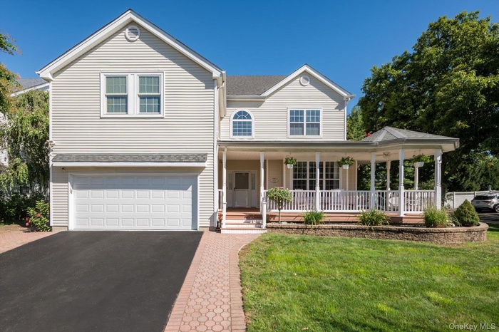 Traditional-style home with a porch, asphalt driveway, a garage, a shingled roof, and a front lawn