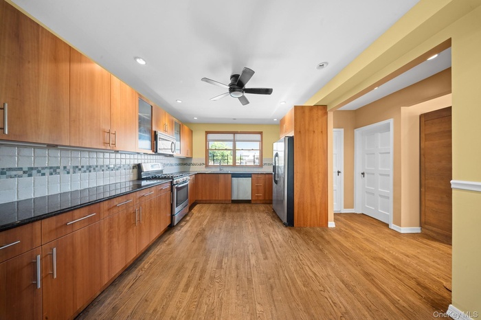 Kitchen with appliances with stainless steel finishes, light wood-style floors, ceiling fan, decorative backsplash, and a sink