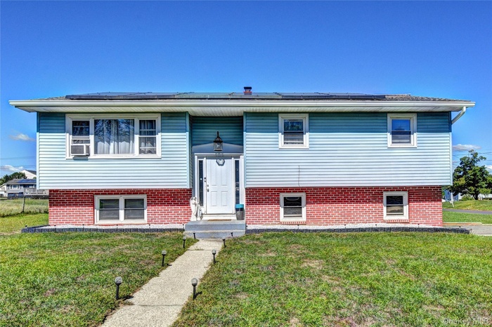 Split foyer home with a front yard, roof mounted solar panels, and brick siding