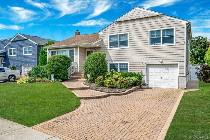 Split level home featuring an attached garage, a chimney, a front yard, and decorative driveway
