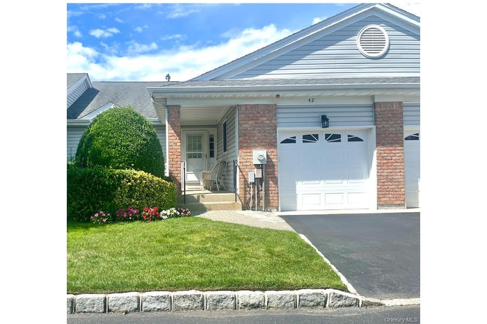 View of front facade featuring brick siding, a front lawn, asphalt driveway, an attached garage, and a porch