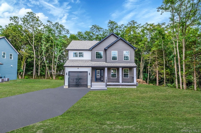 Traditional-style house featuring a shingled roof, asphalt driveway, a porch, a front lawn, and an attached garage