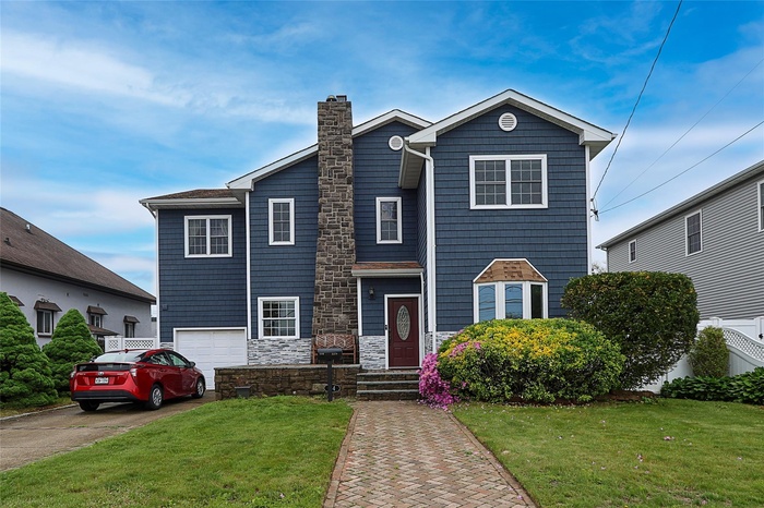 Traditional-style house with a chimney, asphalt driveway, a front yard, an attached garage, and stone siding