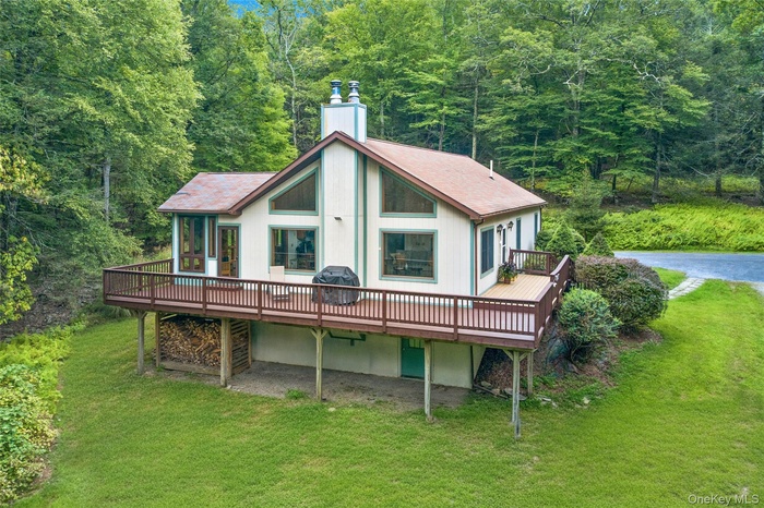 Back of house featuring a deck, a chimney, a yard, and a shingled roof