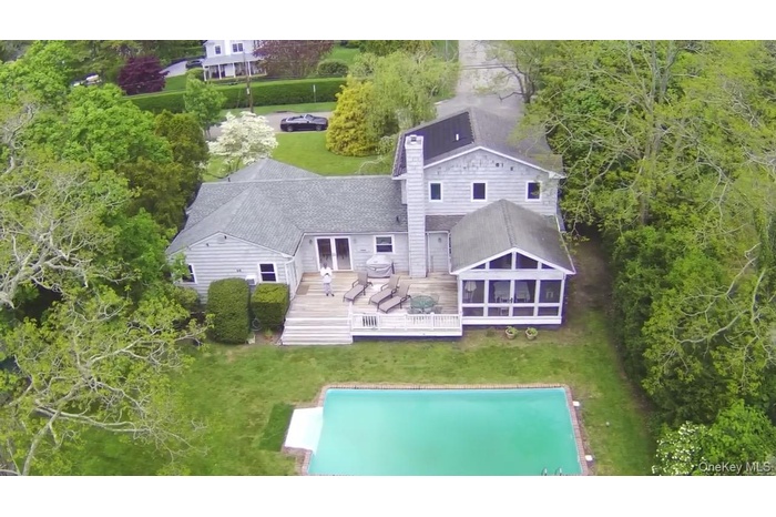 Back of house featuring a deck, a yard, a shingled roof, and a sunroom