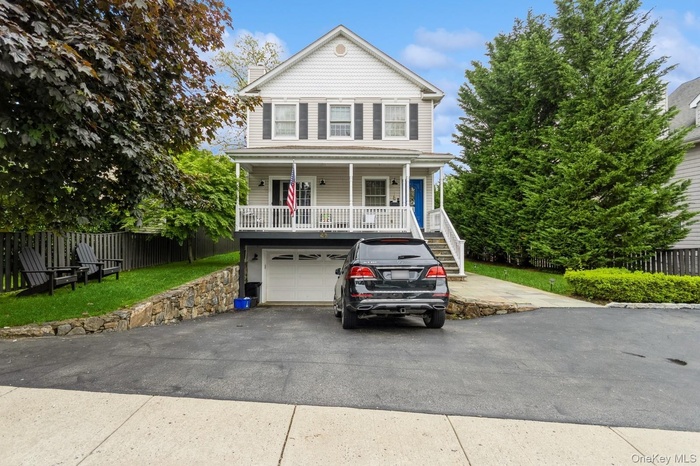 View of front of home featuring covered porch, driveway, stairway, a garage, and a chimney