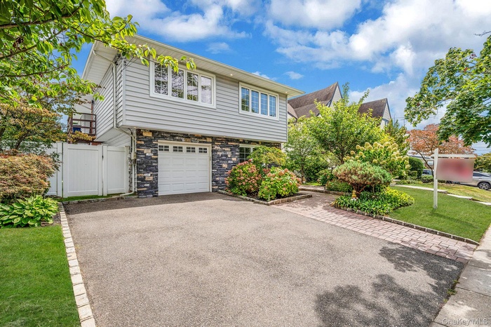 View of front of house featuring stone siding, a gate, an attached garage, and driveway