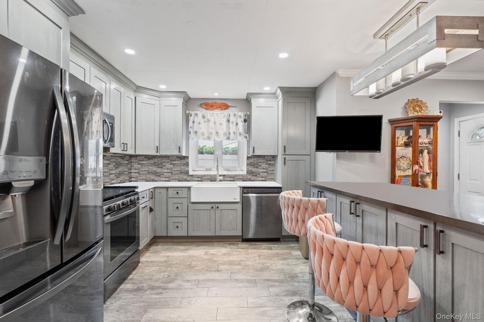 Kitchen featuring appliances with stainless steel finishes, decorative backsplash, recessed lighting, gray cabinets, and light stone counters