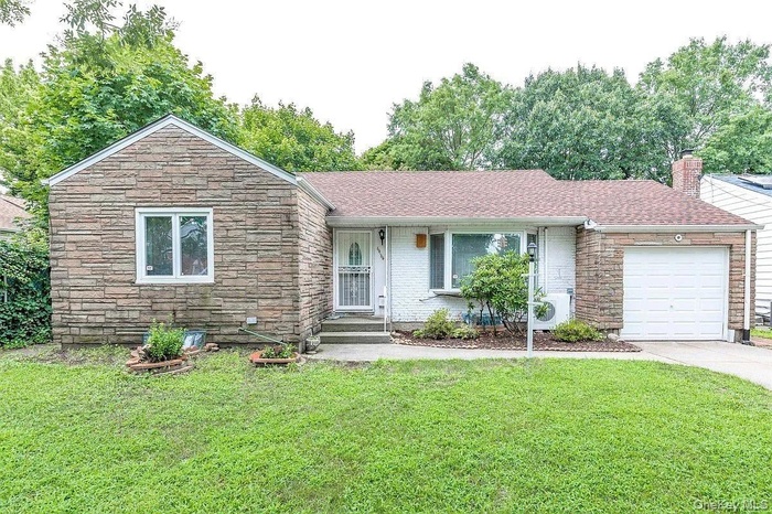 Ranch-style home featuring stone siding, a garage, a front lawn, a chimney, and driveway